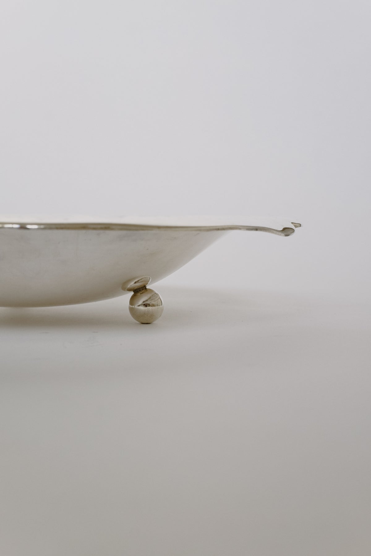 A close-up view of the Silverplated Bowl by septembre studios showcases its minimalist design, highlighted by a spherical support underneath. Set against a plain white background, its unique character and modern appearance shine through.