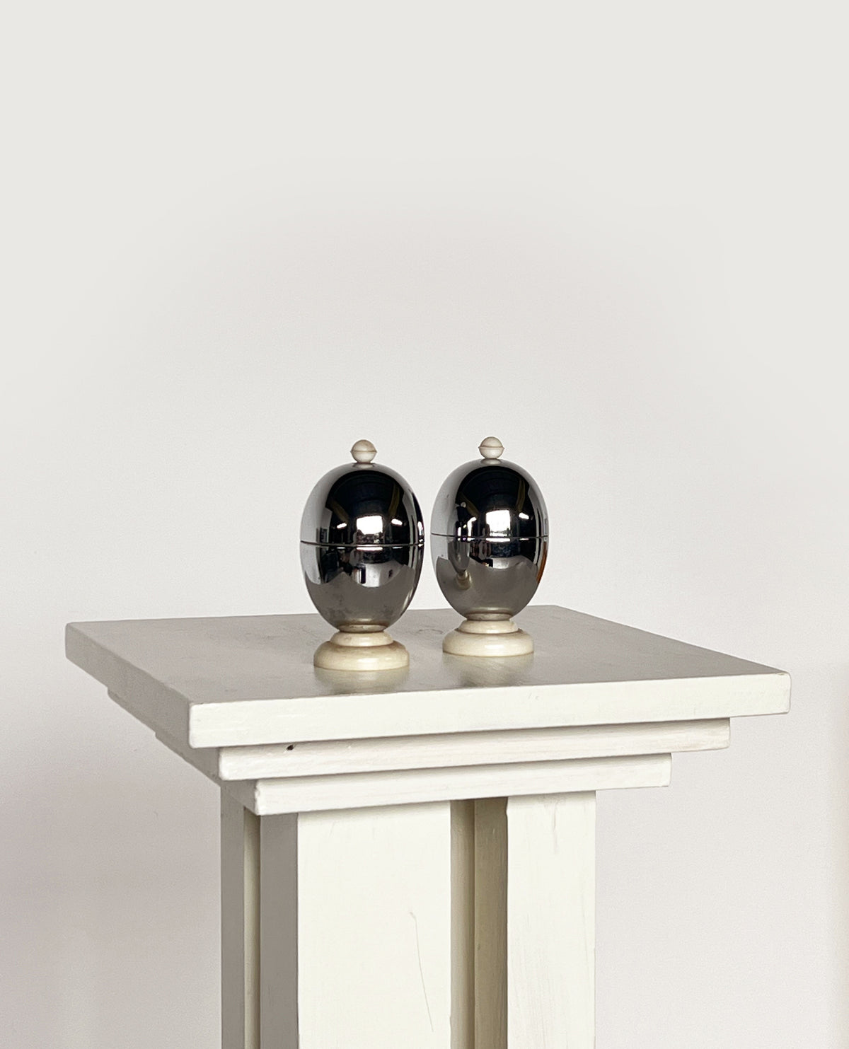 Chrome egg warmers with brass bases on white pedestal table
