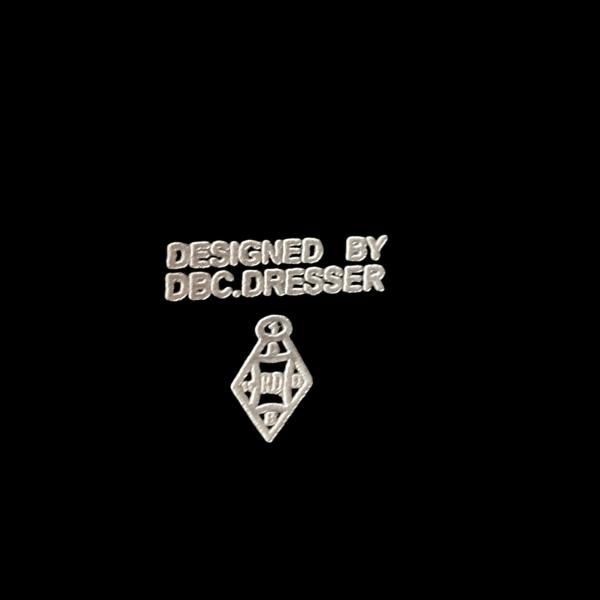 Silver text reads "DESIGNED BY DBC.DRESSER" on a black background, with a geometric emblem featuring diamond shapes below the text, evoking Christopher Dresser's teapot designs. Product: Christopher Dresser Square Teapot by Porter Studio.