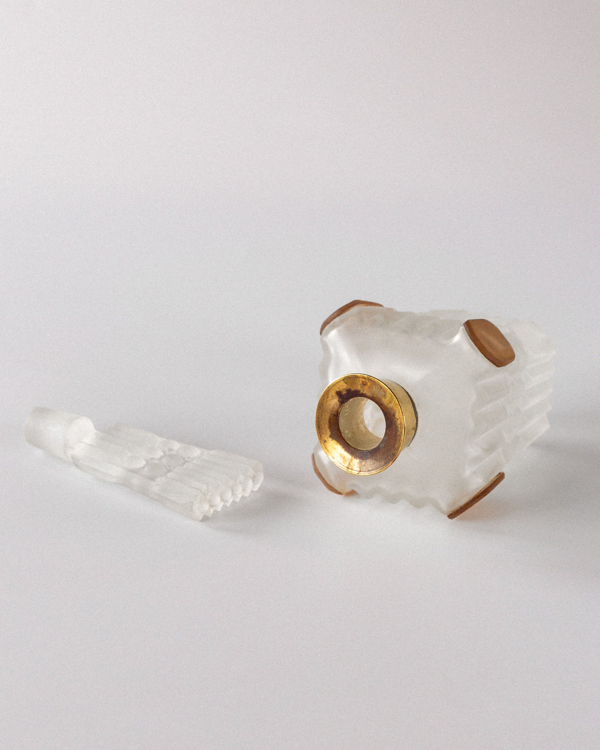 A Spigel Art Deco Perfume Bottle from 1930s France, crafted in frosted glass with gold accents, elegantly lies on its side against a white background. The geometric design is complemented by the matching frosted stopper beside its open neck, exuding timeless elegance.
