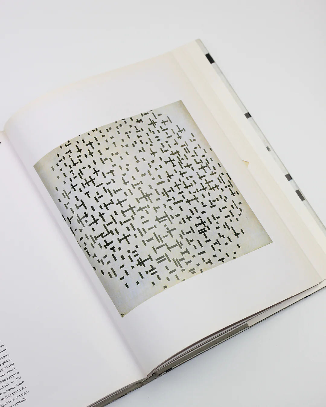 An open copy of "Mondrian" by Hans L.C. Jaffé from Boga Avante Shop displays abstract art in the neoplasticism style, featuring small black geometric shapes on a clean white background, with a hint of text on the opposite page.