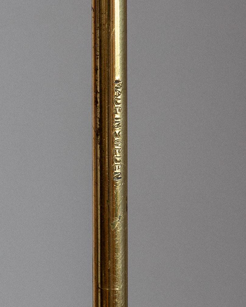A close-up of a metallic object evokes a Swedish Mid-Century Brass Candelabra by Spigel, with "Made in Germany" engraved. Its smooth, slightly worn reflective surface stands against a plain gray background, echoing the elegance of Scandinavian Modern design.