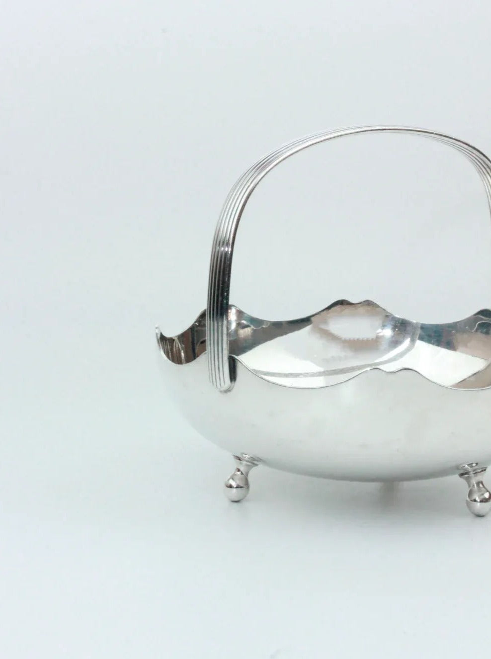 A refined Silver Vintage Basket from Boga Avante Shop, showcasing an elegant and smooth, reflective finish. This beautiful piece features a single curved handle and stands on four small, round feet. The gently scalloped edges provide a decorative touch. Crafted by Meneses Spain, the basket is empty and set against a plain white background.