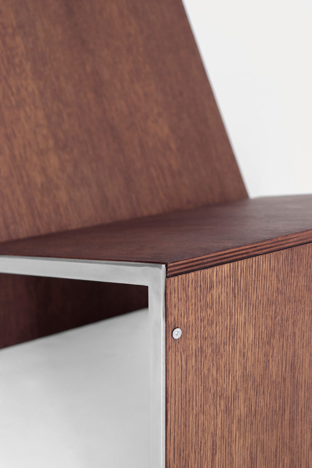 Close-up of the Lounge Chair 2022 by Studio HAOS, featuring a sleek metal frame and smooth wood grain that highlight the chair’s minimalist design and grounded elegance.