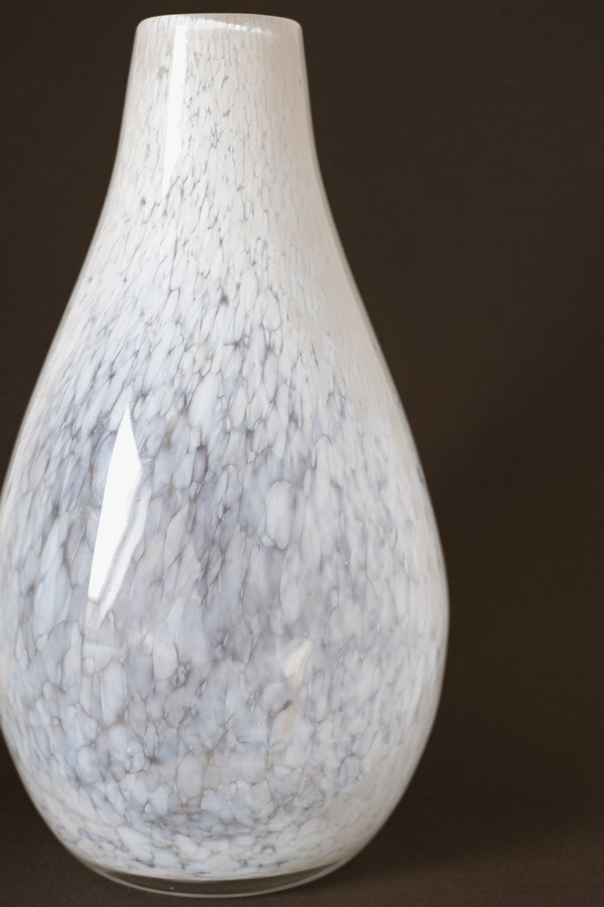 A close-up of the White Vase Tortoise Glass by septembre studios, featuring a white and light gray marble pattern with a glossy finish, is set against a dark background that highlights its unique, vintage character.