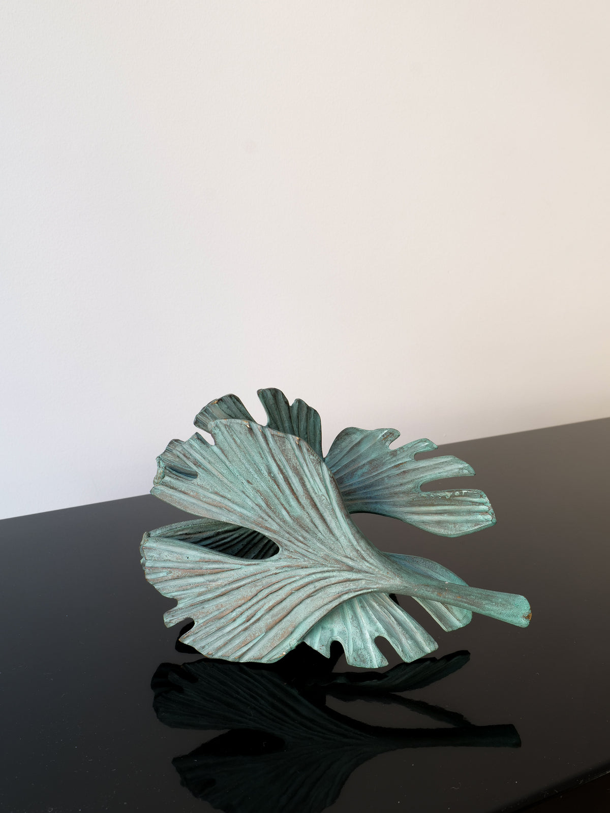 The Bronze Ginko Biloba Sculpture by Collection apart, resembling a stylized green leaf with wavy edges, sits gracefully on a glossy black surface against a plain white background.