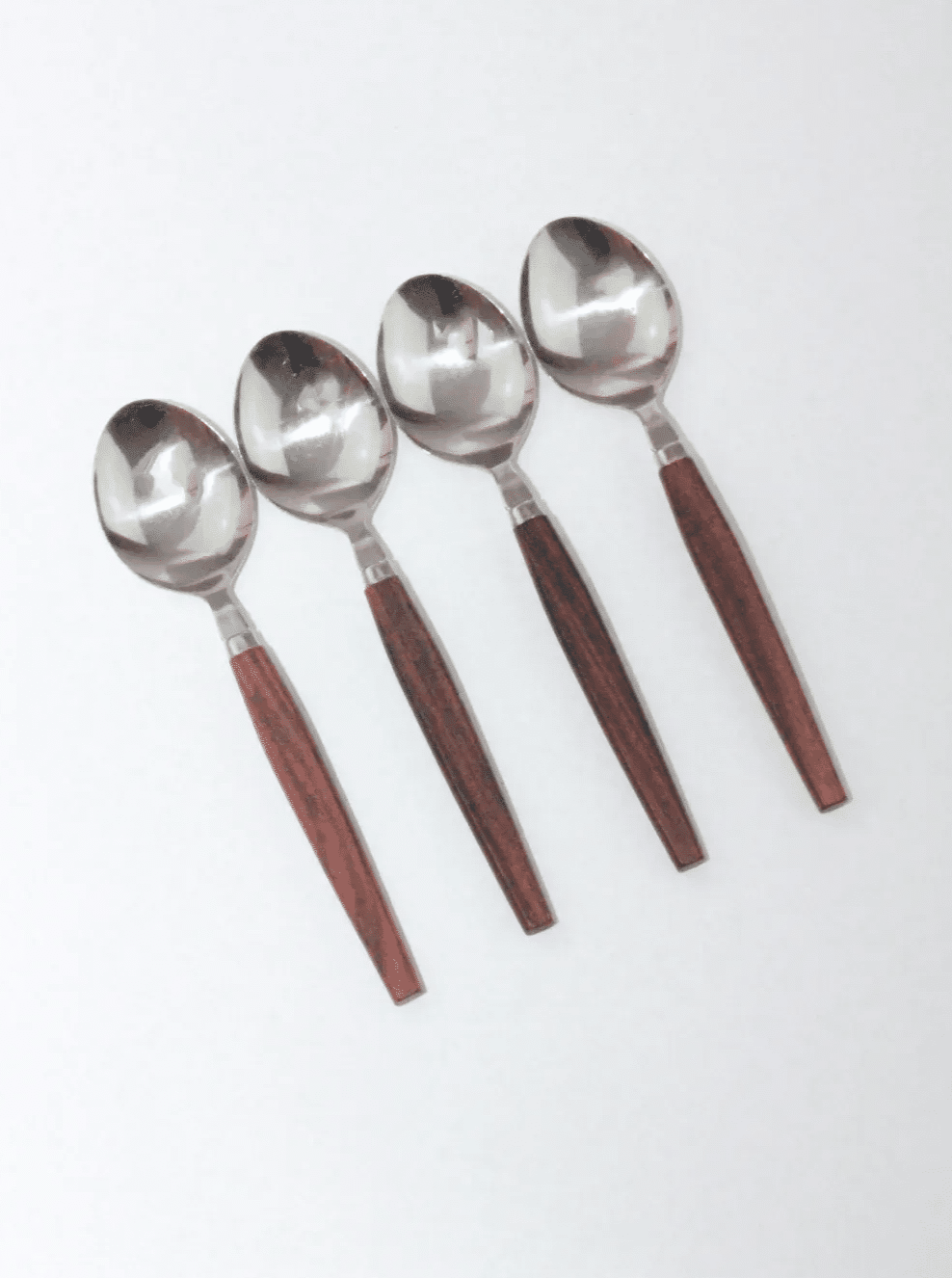 Four Mid-Century Cutlery Set spoons from Boga Avante Shop with rich, teak handles are neatly aligned in a row on a white background, evoking the elegance of mid-century cutlery.