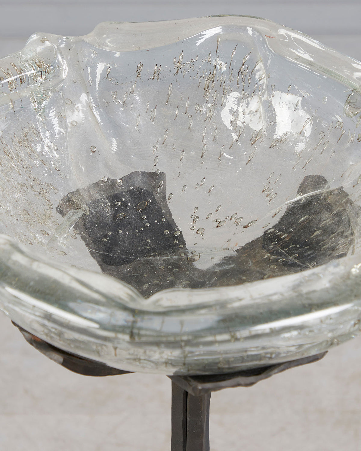 Glass bowl with dark stones on brutalist iron stand detail