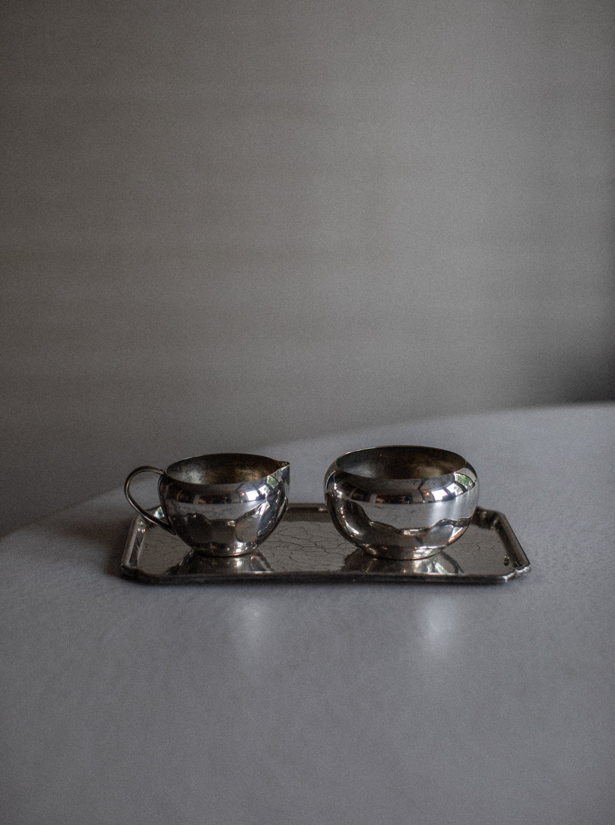 A vintage **Out For Lunch Art Deco Creamer & Sugar Bowl** placed on a rectangular silver tray. Both vessels are reflective with elegant, curved shapes and simple handles, exuding vintage glamour on a light-colored surface against a neutral background.