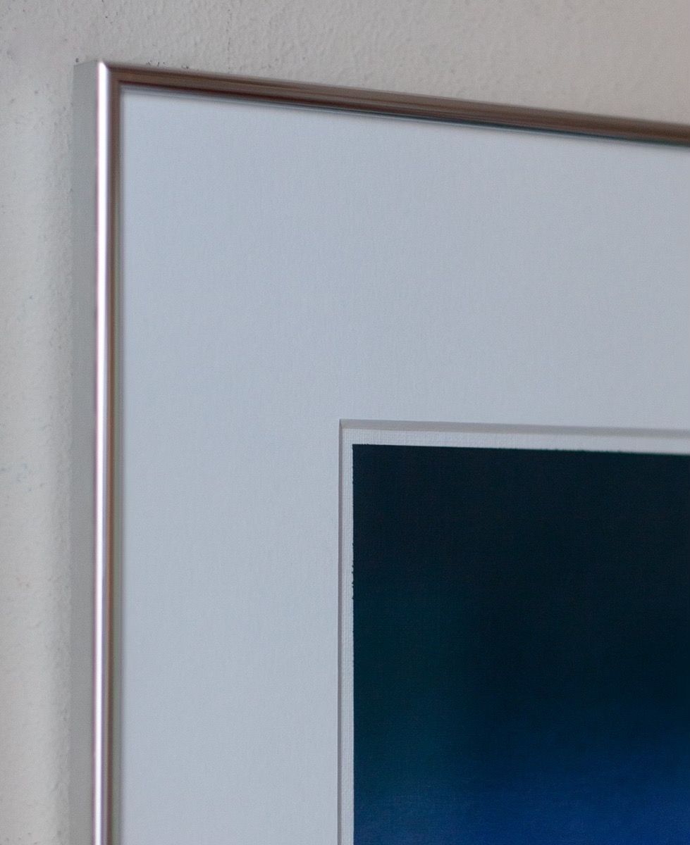 Close-up of "Untitled, 2024" by Rebecca von Matérn, highlighted by a sleek aluminium frame. The visible section reveals a gradient of dark blue reminiscent of an acrylic painting. It's mounted on a light-colored wall that complements its modern appeal.