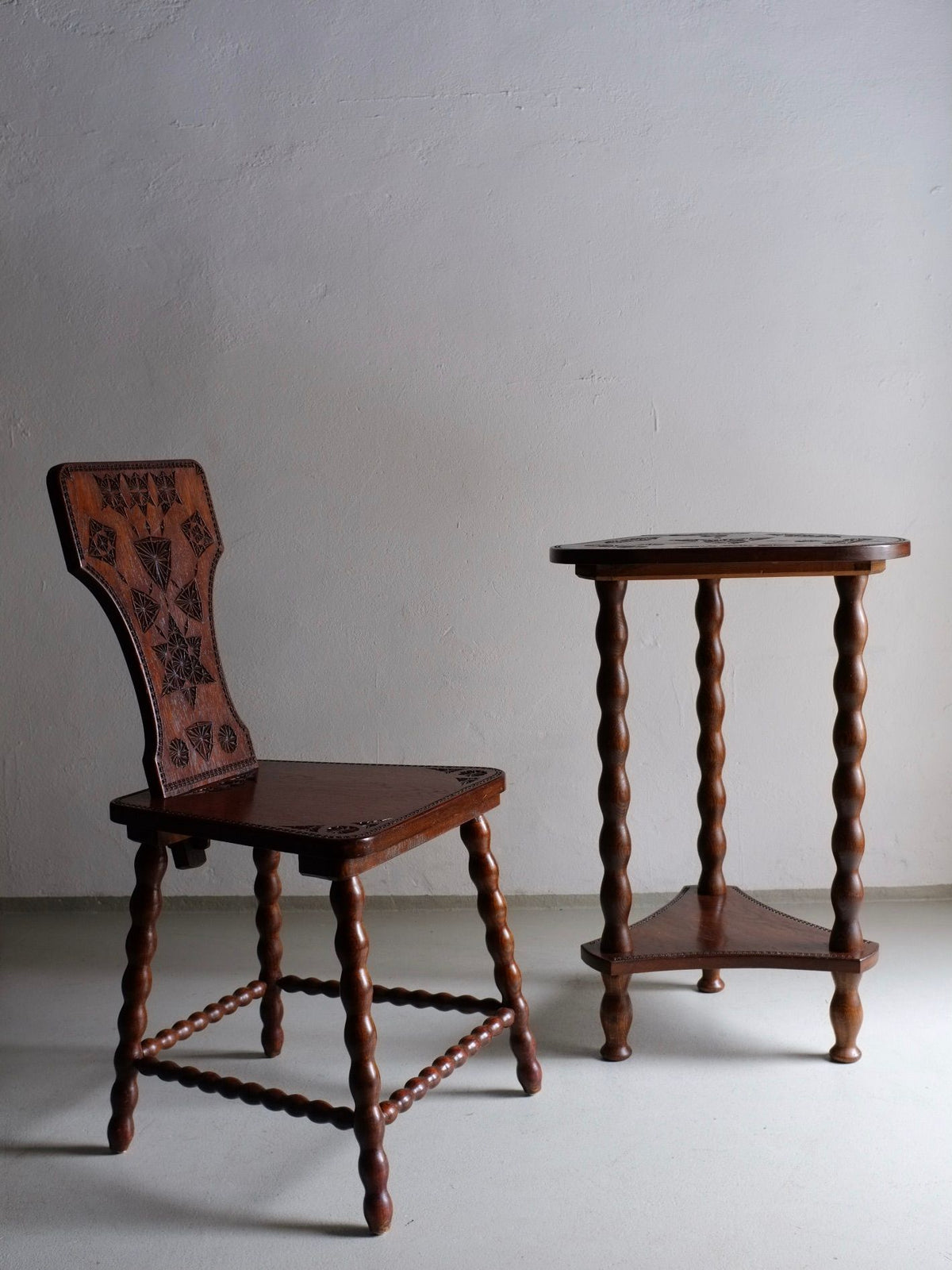 A Carved Wood Bobbin Chair and Table Set by Veter Vintage, reminiscent of 1960s design, stands next to a table set featuring a small wooden table with spiral-turned legs. The furniture is set against a plain off-white wall.