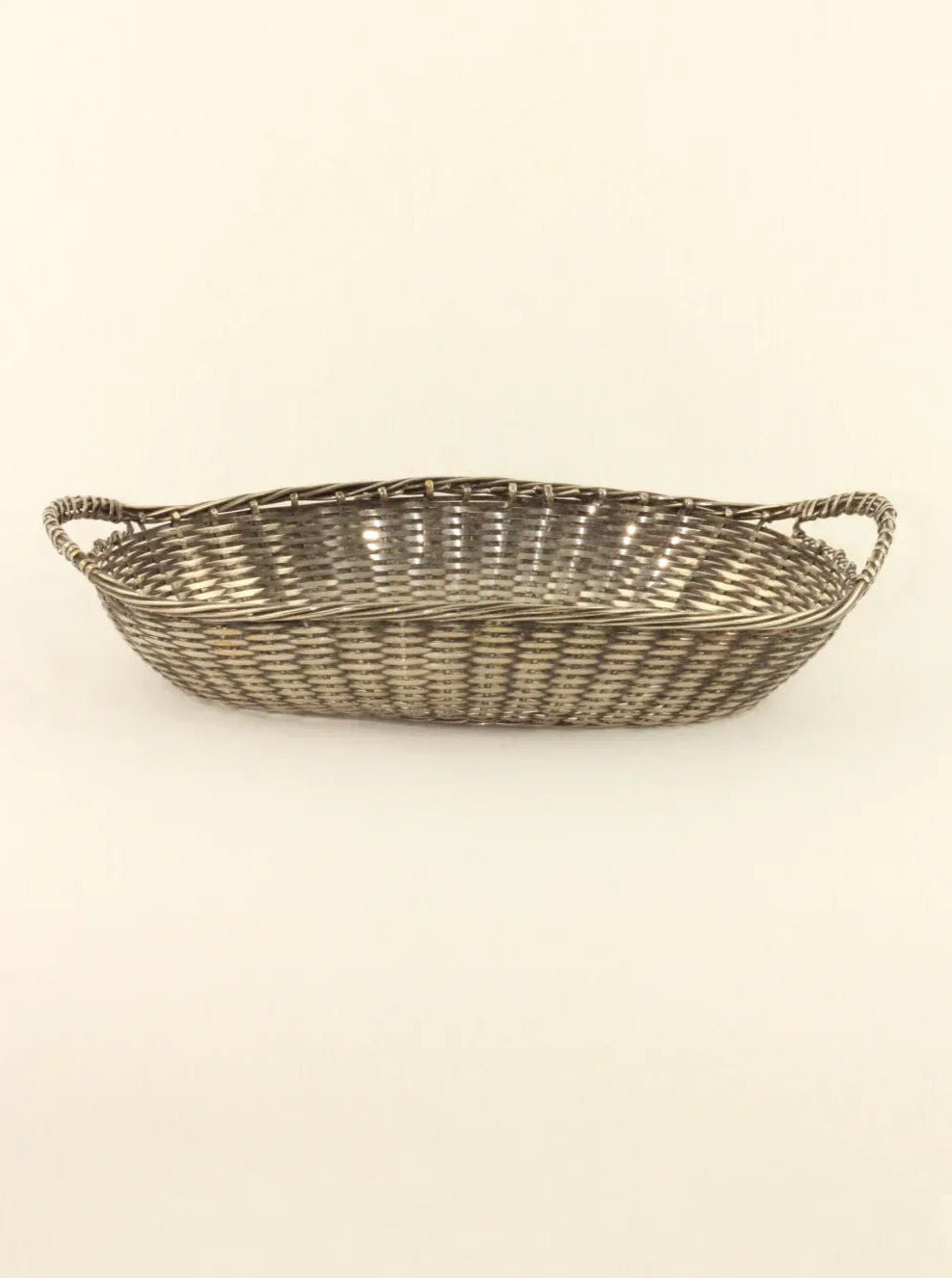 A shallow, hand-woven Woven Basket with rounded edges and a checkered geometric pattern. The rectangular wicker design showcases a natural color palette and features two handles on either end for carrying. Accents of silver-colored brass add a touch of elegance against the neutral, uncluttered background. Available at Boga Avante Shop.