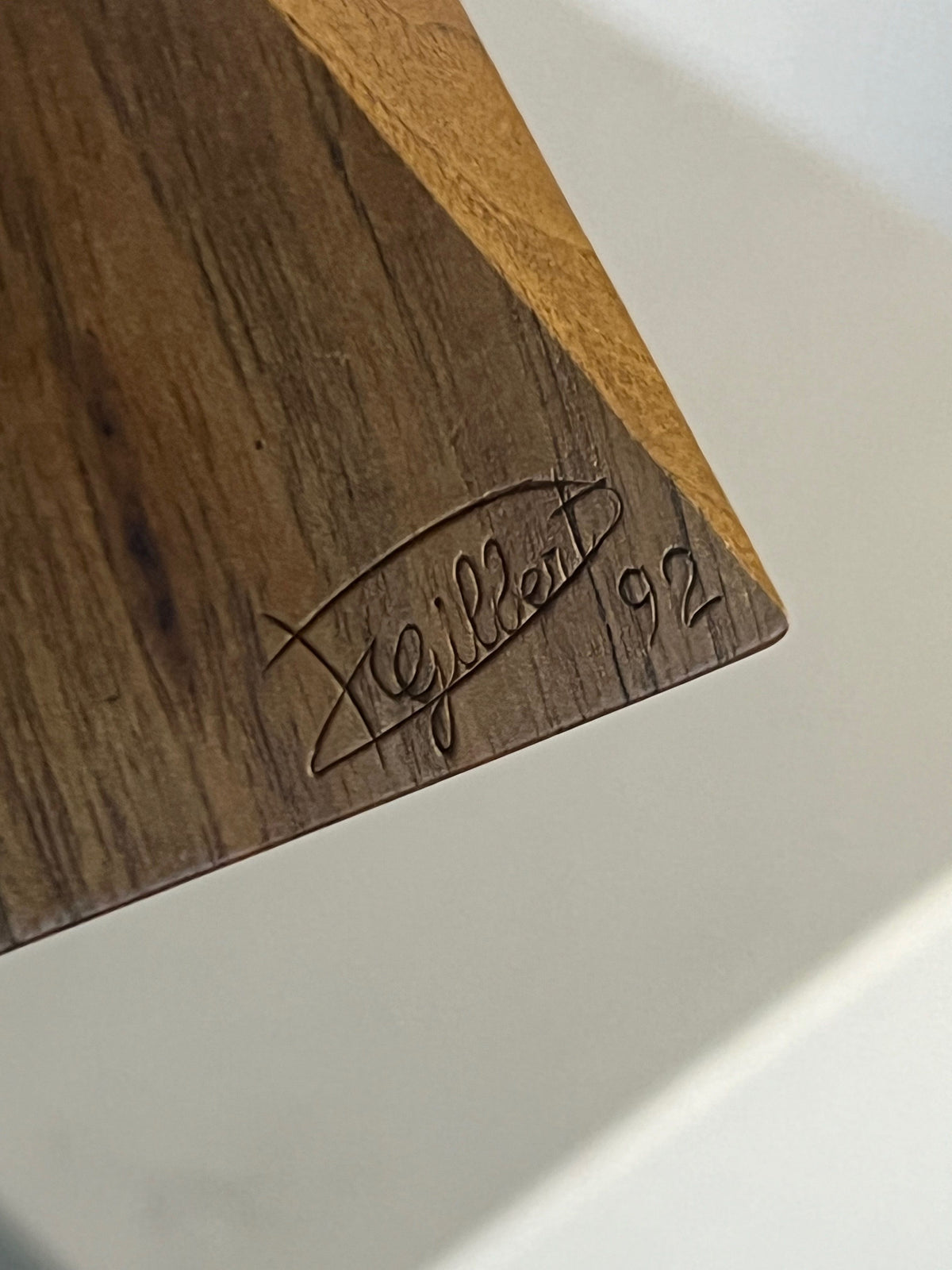 Close-up of a wooden corner featuring Philippe Gilbert's carved signature and the number '92.' The Yin Yang Orb sculpture from Porter Studio showcases natural wood grain and a triangular shape, where light and dark sections blend seamlessly at the corner.