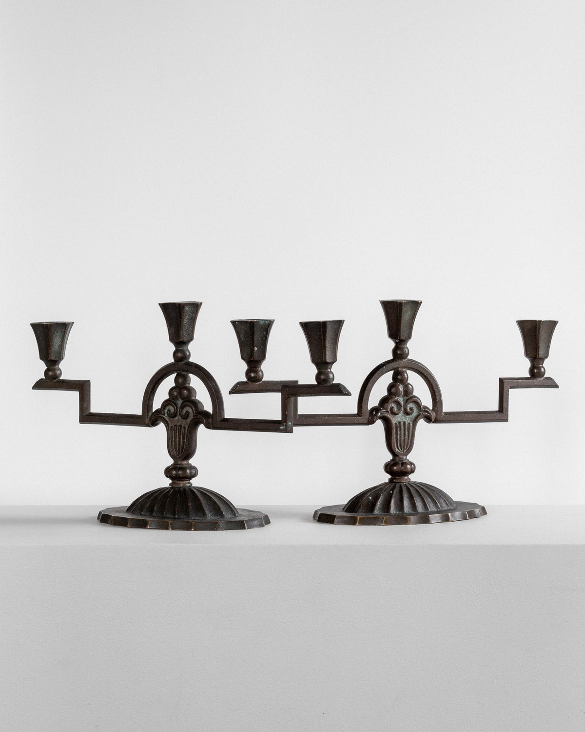 Two ornate, vintage-style Art Deco Bronze Candelabras from the 1930s, each with three candle cups, are displayed against a plain white background. Crafted by Spigel, these solid bronze candle holders feature intricate designs and are symmetrical with a sturdy base.