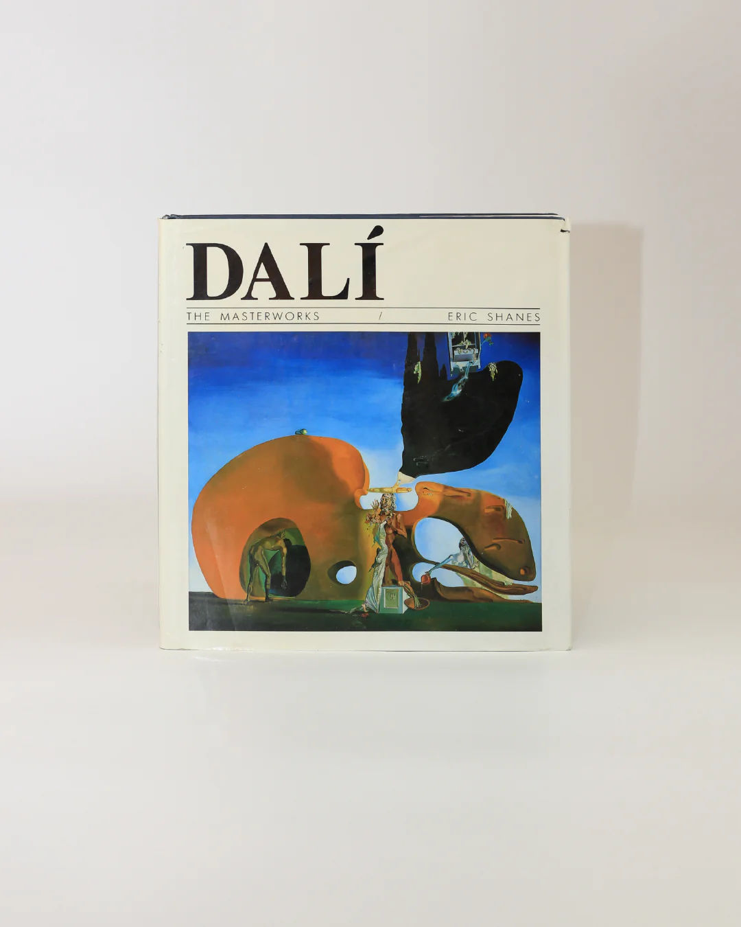 The Boga Avante Shop's "Dali The Masterworks Book" by Eric Shanes features a cover depicting a surrealist dreamscape with abstract shapes in vivid orange and dark blue, set against a tranquil blue sky, capturing the spirit of modern art.