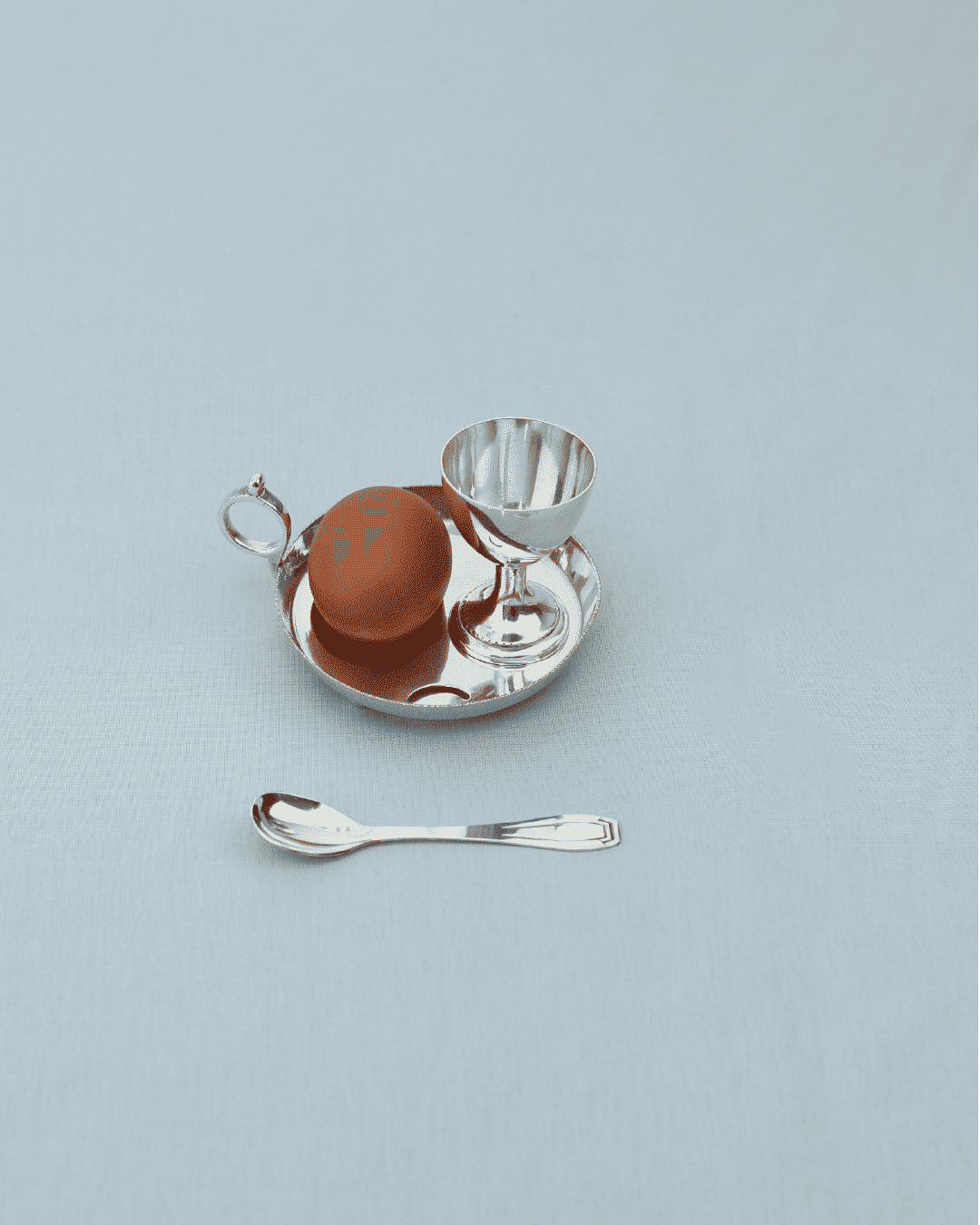 Silver-plated egg cup with serving tray and spoon on white