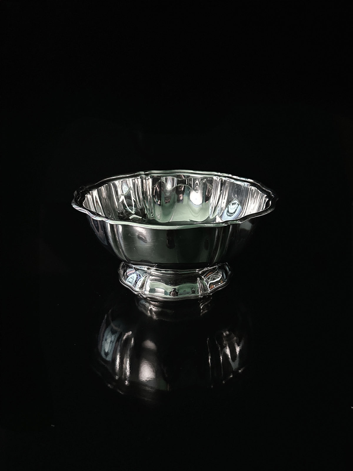 A reflective silver bowl with intricate designs from the Dodo Vintage Italian Stainless Steel Dessert Coupe Set sits on a dark surface, showcasing its scalloped edge and elevated base against the black background.