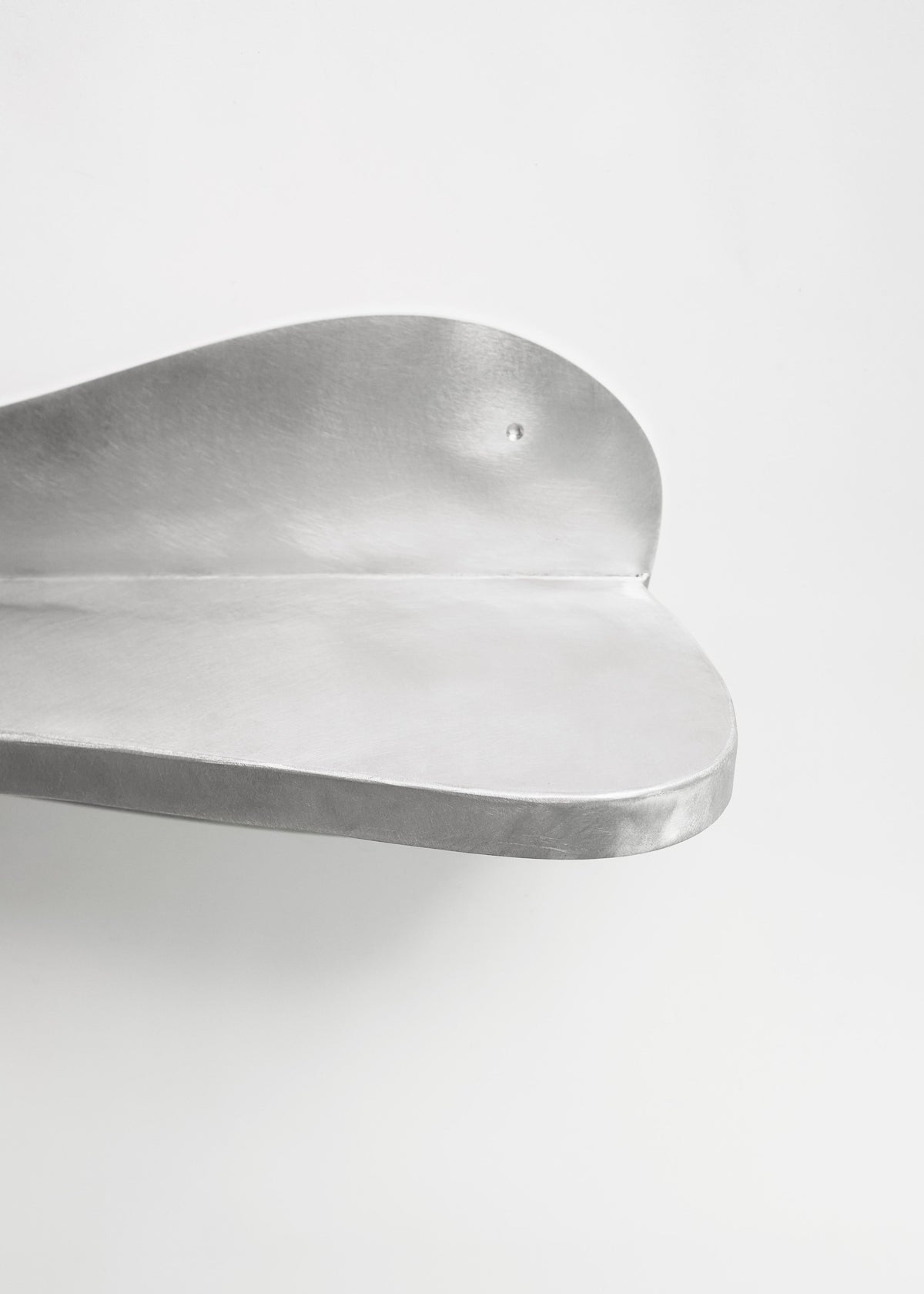 The Big Shelf by Six Dots Design is a sleek, minimalist silver piece with smooth curves, resembling modern art. Set against a plain white background, its metallic surface exudes elegance, making it an ideal curated focal point for any room.