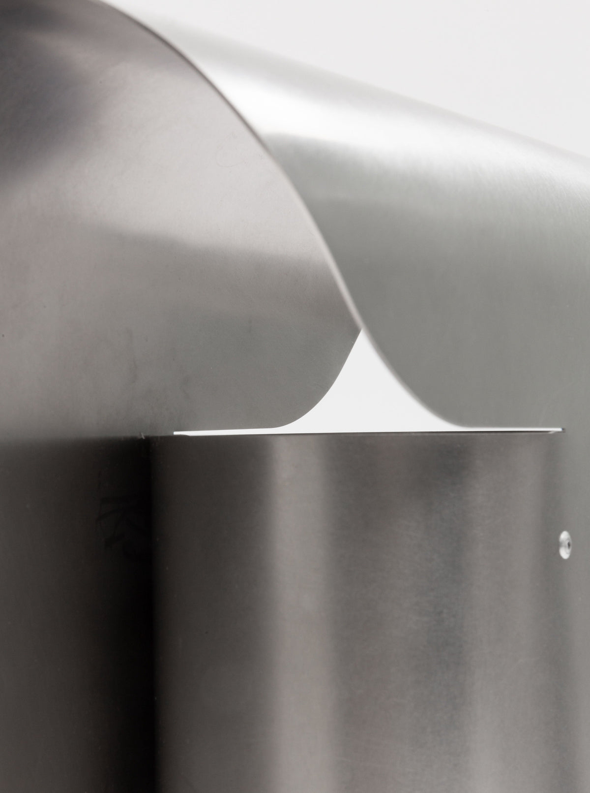 Close-up of a sleek, modern metal sculpture featuring smooth, curved surfaces and minimalist design. Crafted from stainless steel, the overlapping elements and polished finish create a sense of fluidity and sophistication. This is the Arc Table Lamp by Paul Coenen.