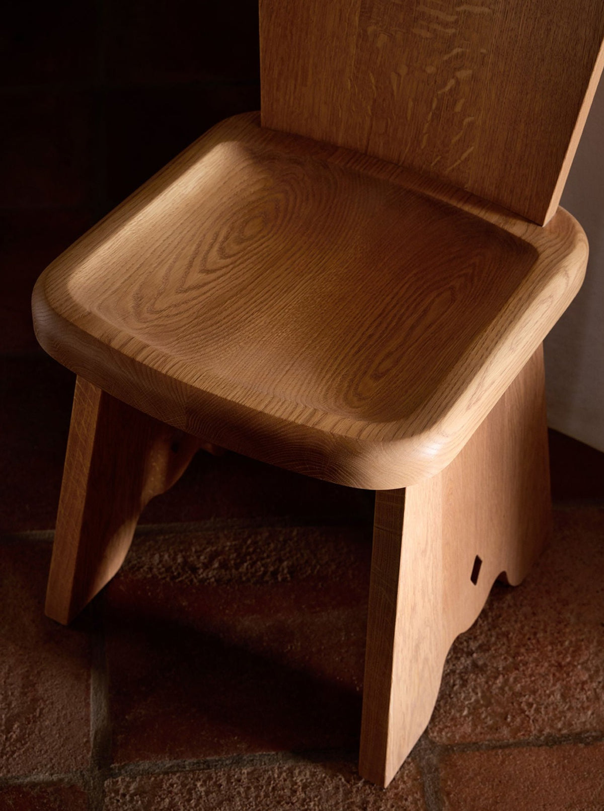 Close-up of the Rambling Chair in Natural French Oak Wood by Lemon with a minimalist design, showcasing the seat and part of the backrest. The chair sits on a tiled floor, and its natural wood grain and craftsmanship are prominently visible. The image highlights the chair's texture, color, and utilitarian functionality.