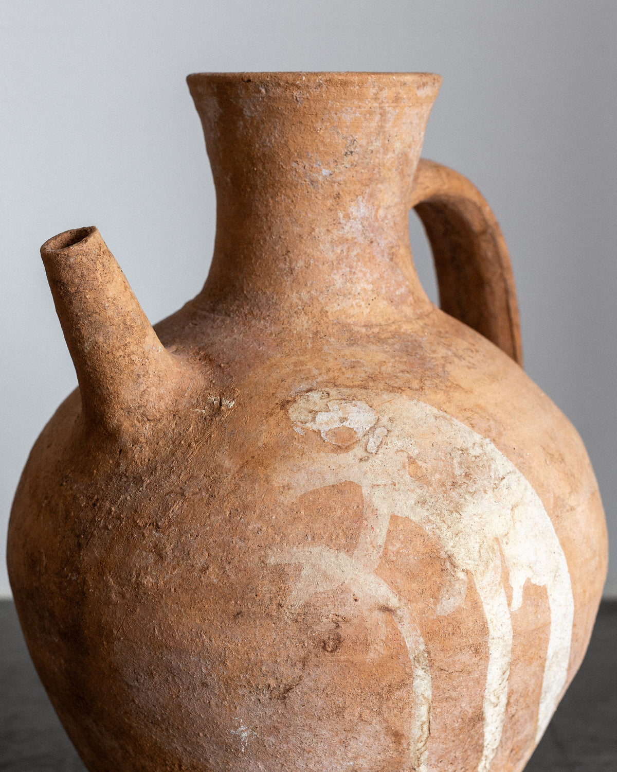 The Early 20th Century European Ceramic Pitcher by Spigel is an ancient, hand-crafted piece with a single handle and spout. It features a faded white pattern on a plain light grey background, perfect for decorative display.