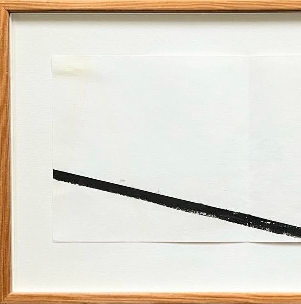 The Richard Nonas Original Lithograph by Médecine features a minimalist design with a black diagonal line running from the bottom left to the upper right on a white canvas. This artwork, likely drawing inspiration from post-minimalist art, is beautifully encased in an elegant light wooden frame.