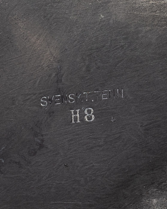 Close-up of a metallic surface with the text "Spigel" engraved on it, reminiscent of an Art Deco Metal Box from 1934. The engraving is slightly worn, and the surface boasts a textured, aged patina that adds to its charm.