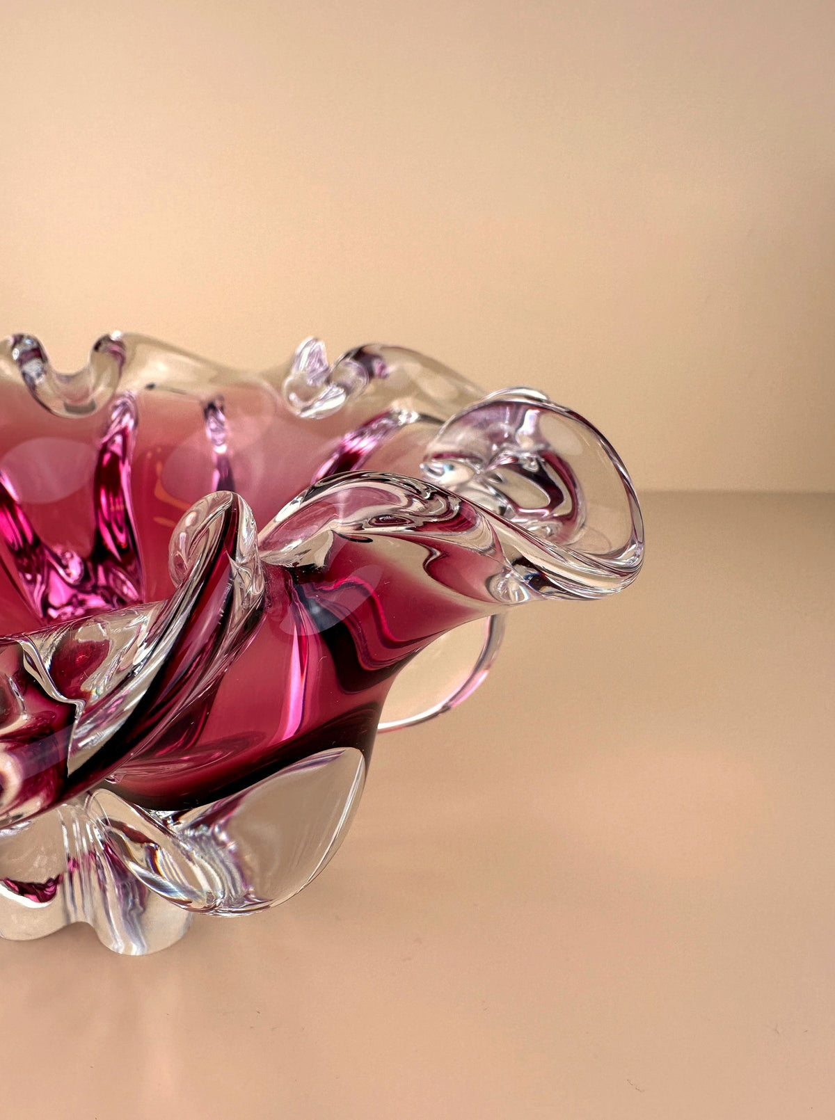A Bohemian Cranberry Red bowl by Josef Hospodka, crafted by Dodo Vintage glassmakers with swirling pink and clear patterns, resting on a soft beige surface with a matching background.
