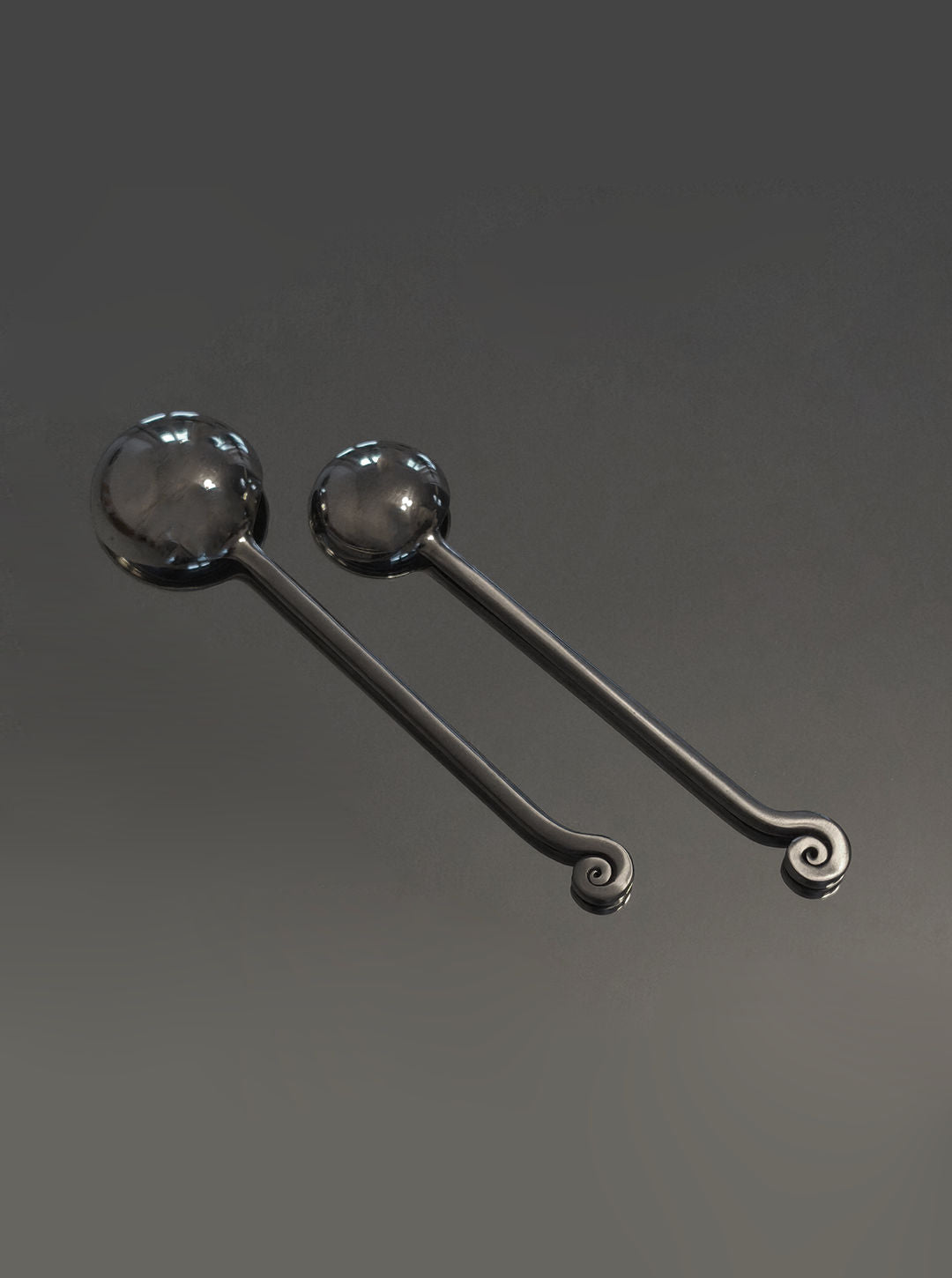 Two polished stainless steel serving spoons with spiral handle ends
