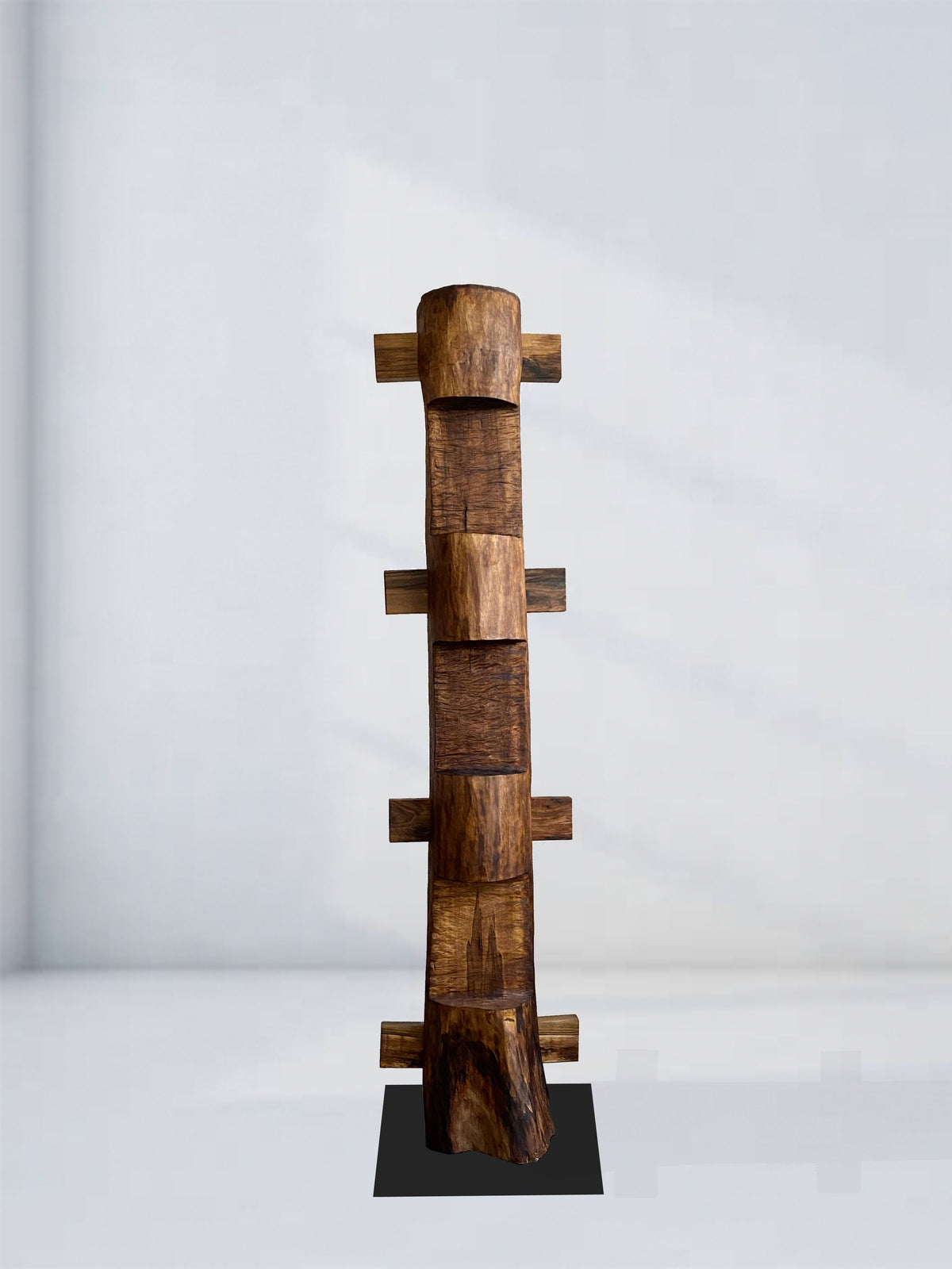 The 'Die Nacht' Sculpture by Eloi Schultz is a tall, vertical walnut totem with staggered rectangular blocks and mortise and tenon joints, standing on a black base against a plain background. Each piece is made to order.