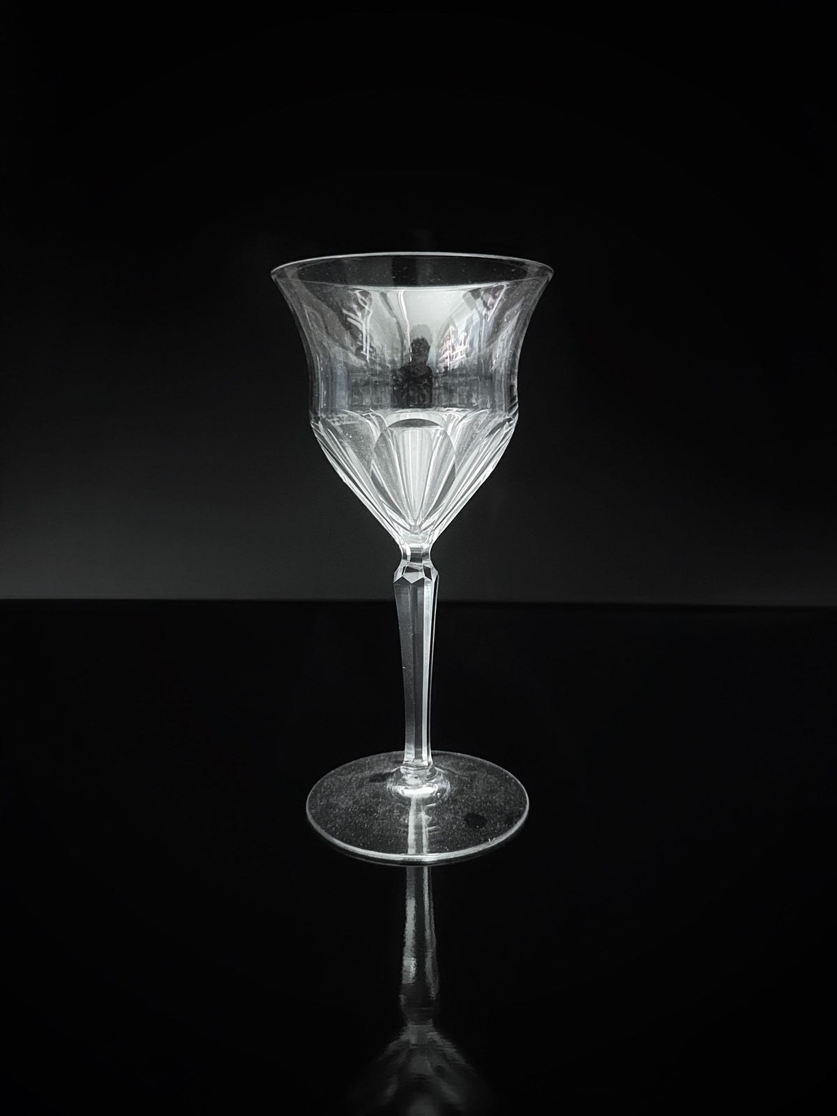 The Dodo Vintage 9 Hand Cut Crystal Wine Glasses from the 1960s feature a transparent, fluted design that showcases exquisite craftsmanship. Set on a dark, reflective surface and contrasted against a black background, they highlight the intricate detailing of fine crystal cut glass.