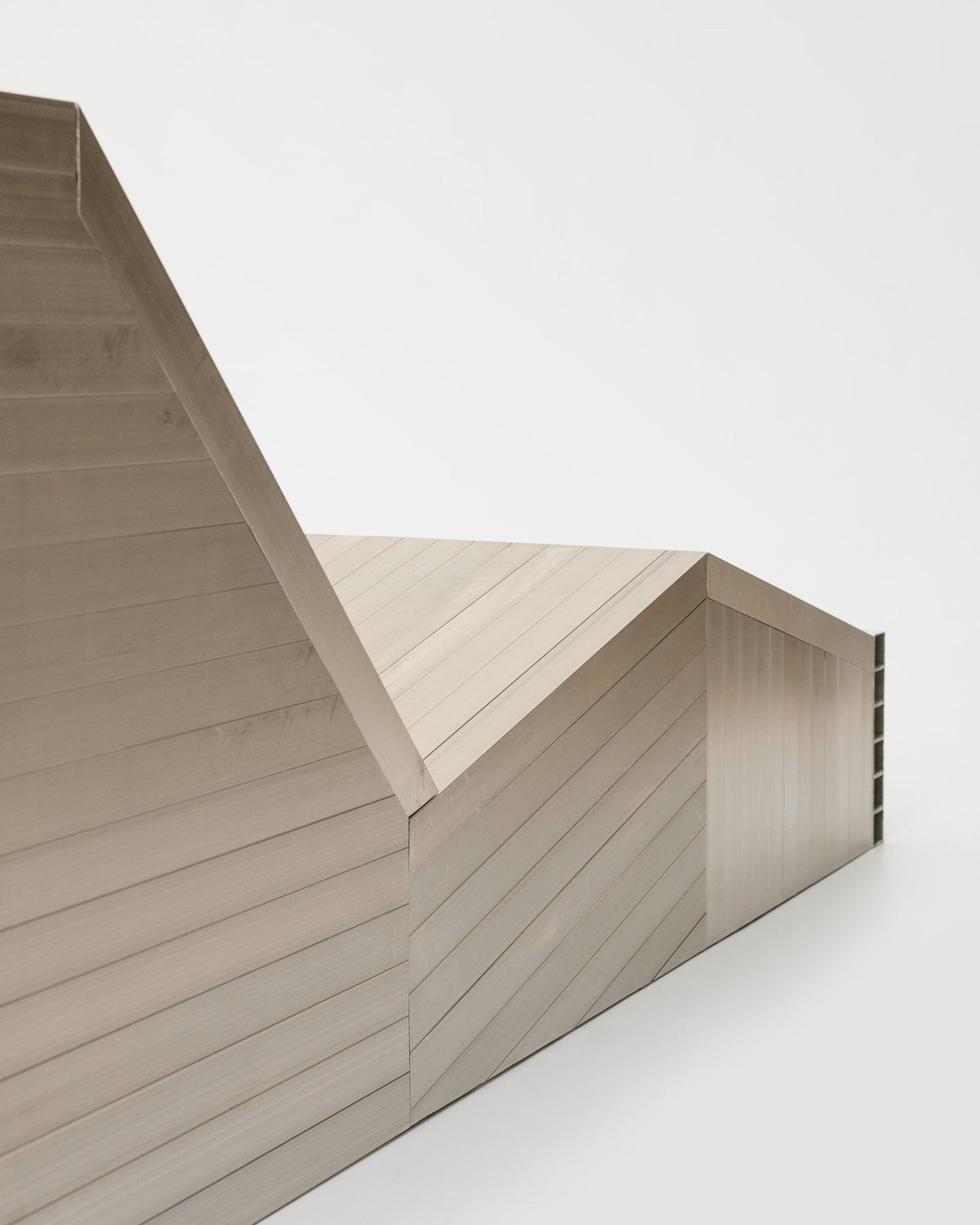 The Aluminum Lounge Chair by Studio HAOS features intersecting angular planes and diagonal lines, creating a minimalist, abstract architectural form set against a plain white background.