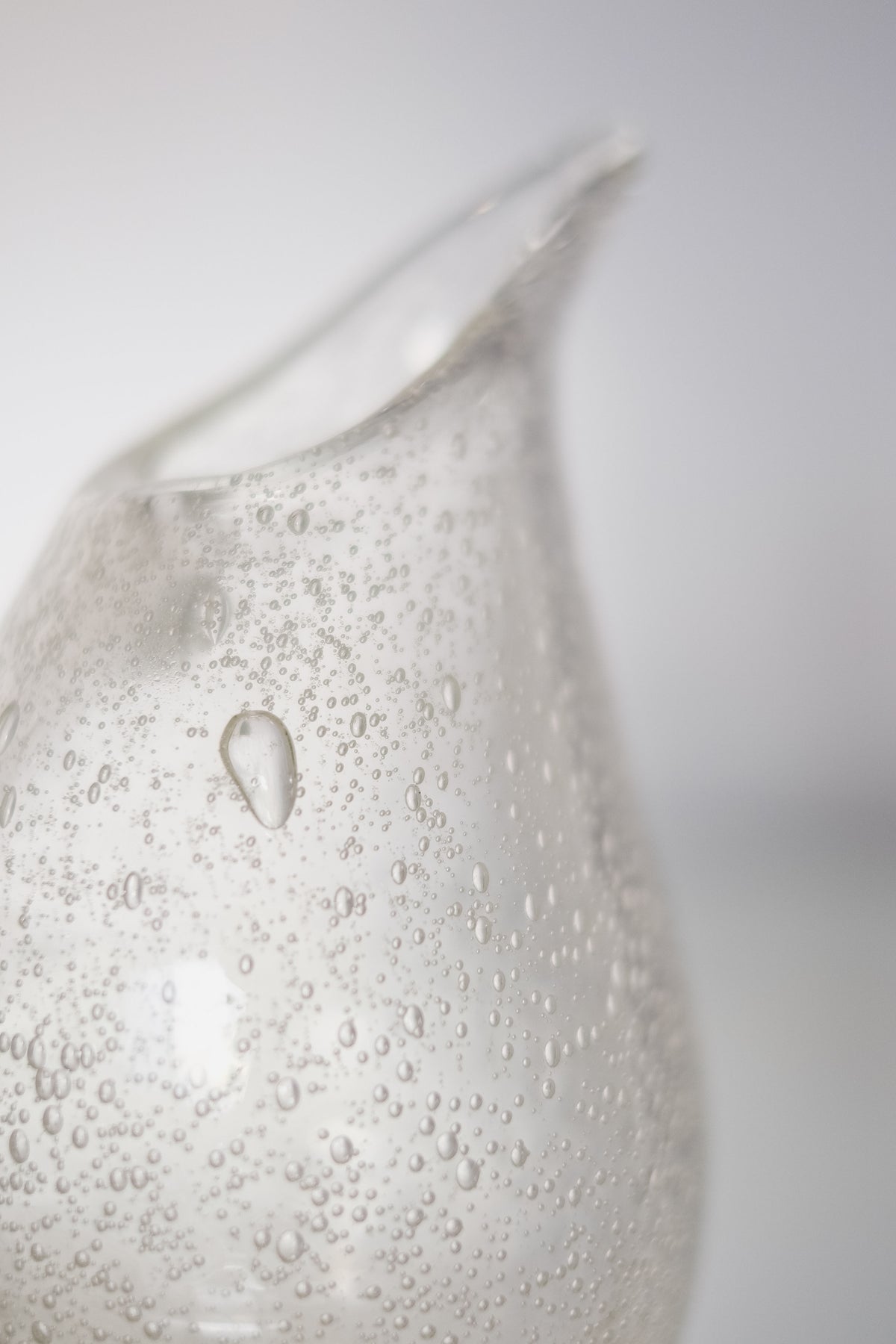 Close-up of the exquisite Small Bubble Vase by septembre studios, featuring small bubbles with a curved spout. Its clear, smooth surface is beautifully translucent against a light and neutral background.