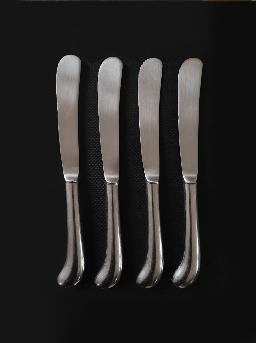 Les Objoies's Set of 4 Butter Knives, featuring sleek rounded stainless steel handles, are artfully displayed side by side on a black background, adding modern elegance to any table.