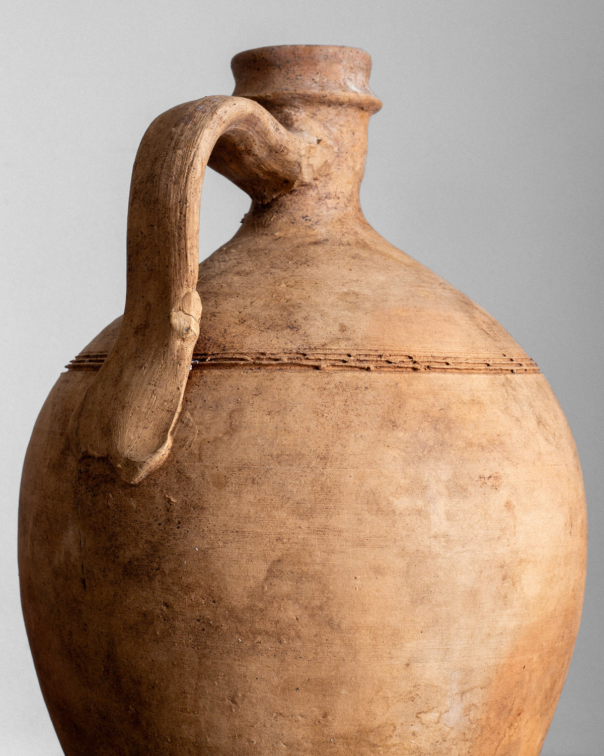 Close-up of an Early 20th Century European Olive Jar by Spigel featuring a rounded body, narrow neck, and single curved handle. The earthenware jar has a textured, earthy brown surface with imperfections, showcasing historical craftsmanship against a plain gray background.