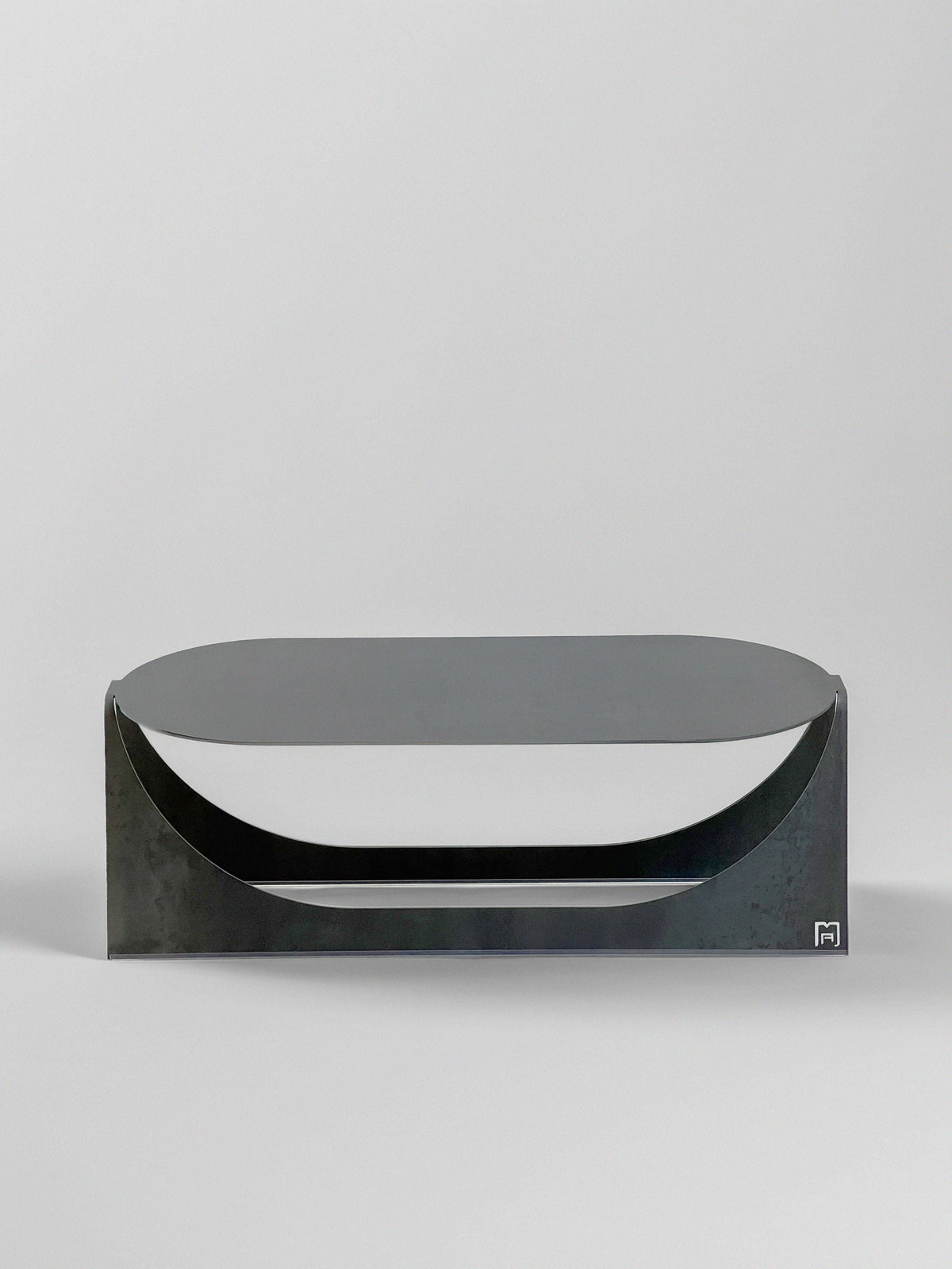 The 'Tani' Coffee Table by Modan is a modern, minimalist black metal piece with a flat top and curved cutout details on the front, crafted from steel plate, shown against a plain white background.