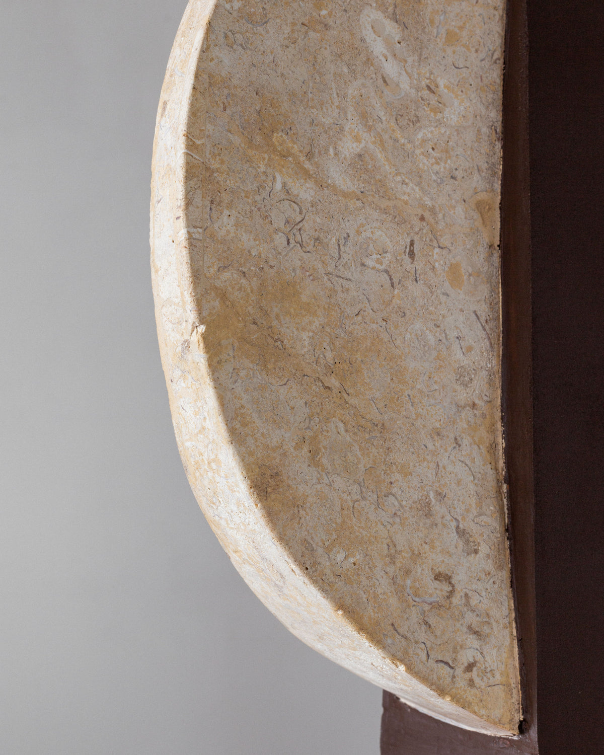 A close-up of the Pair of Large Travertine Table Lamps by Spigel from the 1970s shows a textured travertine base with natural beige and darker pattern contrasts, partially embedded in a dark wall, echoing vintage lighting styles.