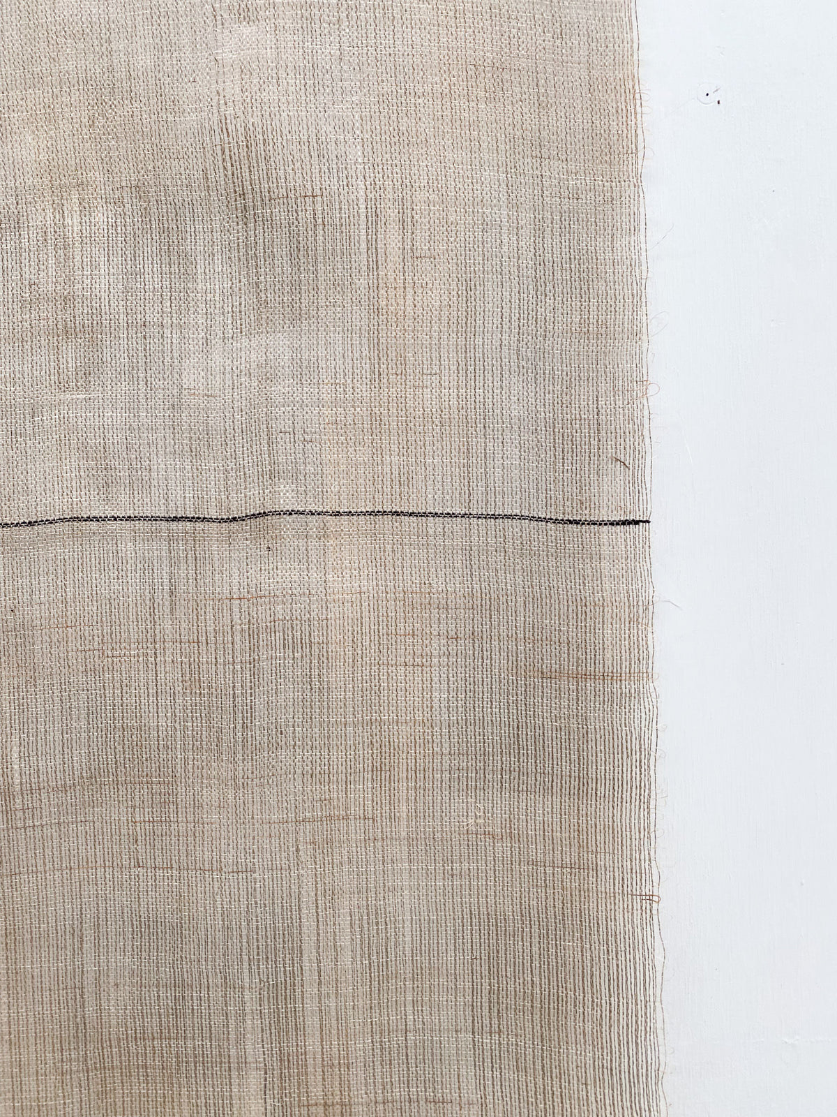 Close-up of Sundance Studio's Distant Horizon fabric in light beige, featuring a horizontal black thread reminiscent of wide open spaces. The slightly rough texture with vertical weaves evokes the natural beauty found near Yaegl Country, set against a white background for simplicity.