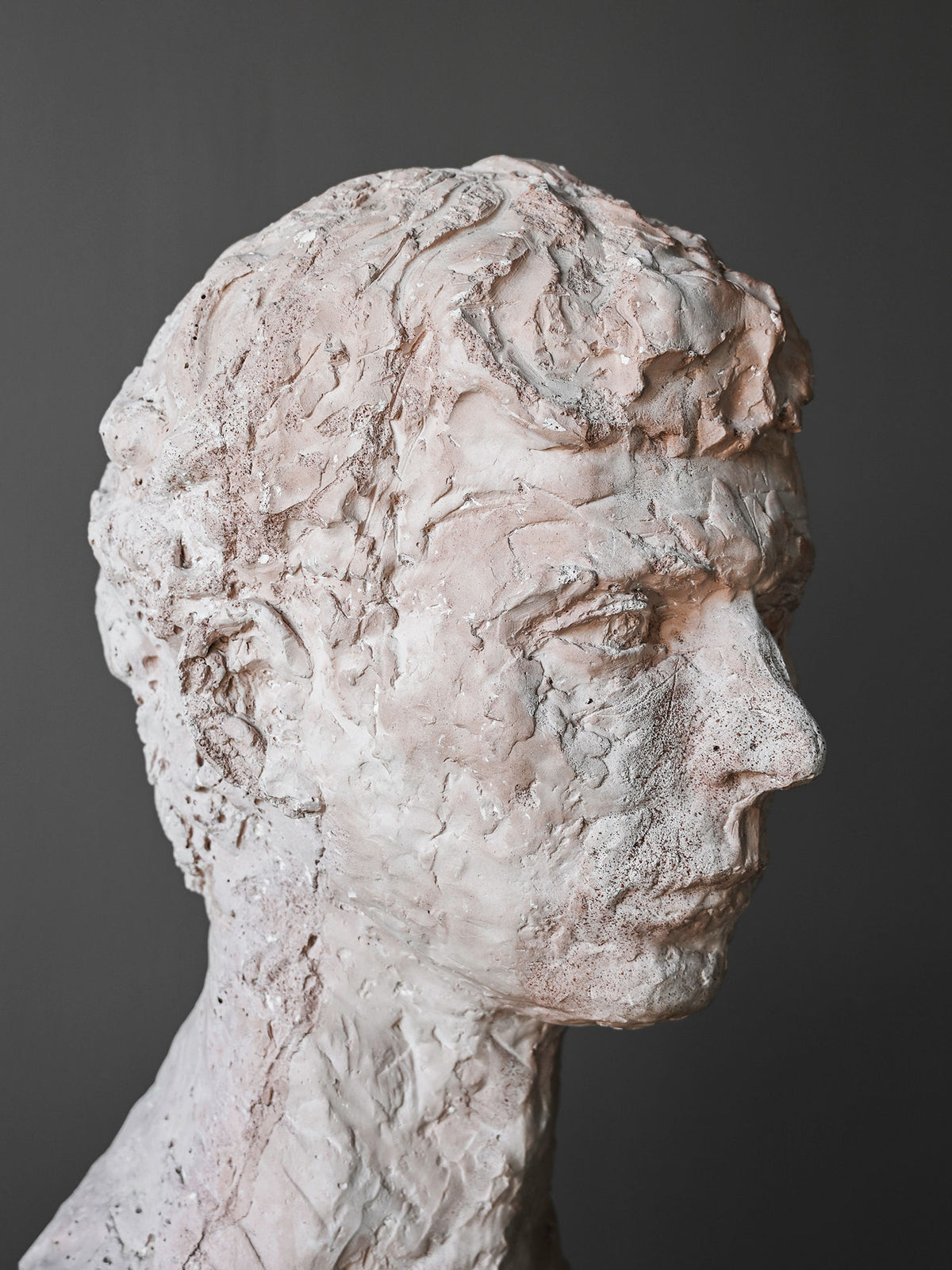 A close-up of the “A Simple Man” Sculpture by Studio OSKLO shows its textured white plaster surface and visible brushstrokes, capturing the essence of 1920s American Folk-Art against a dark gray background.