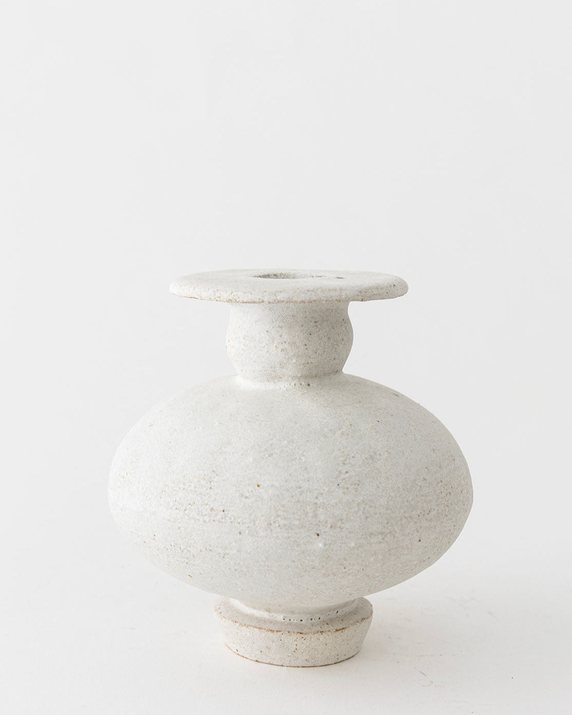 The Calpide Blanco Hueso by Canoa Lab is a round, off-white ceramic vase with a wide body, narrow neck, and flared rim. Its textured, rustic surface recalls Mediterranean design and the timeless appeal of ancient artifacts.