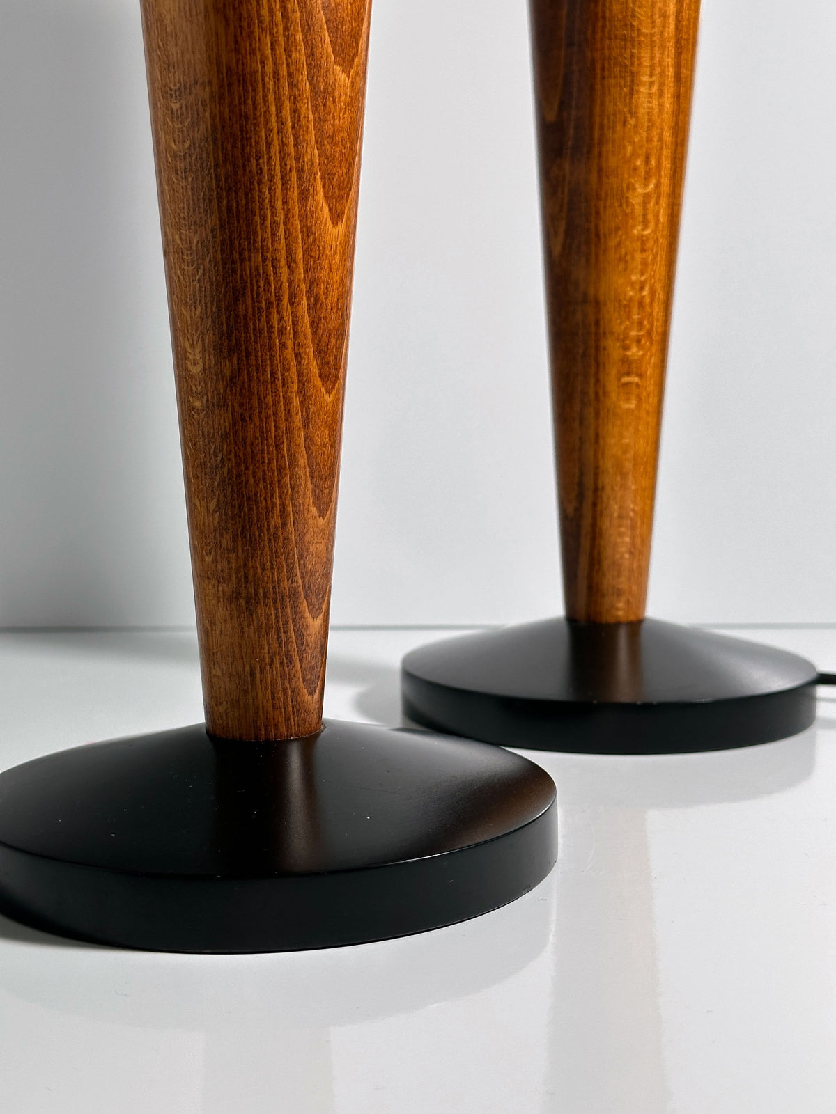 The Pair of Art Deco Chalices with Teak Wood by Dodo Vintage features two richly finished wooden legs mounted on round black bases. The reflective surface and white background accentuate the texture and color, evoking the style of classic Art Deco lamps.