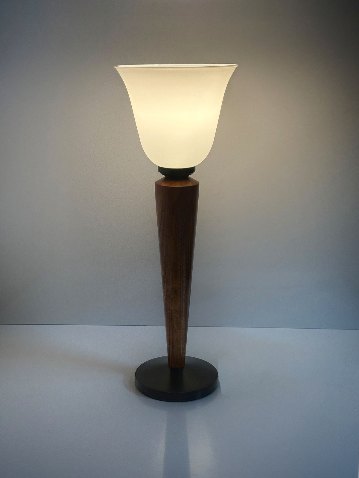 A Pair of Art Deco Chalices by Dodo Vintage, featuring teak wood, casts soft light with a frosted glass conical shade against a gray backdrop.