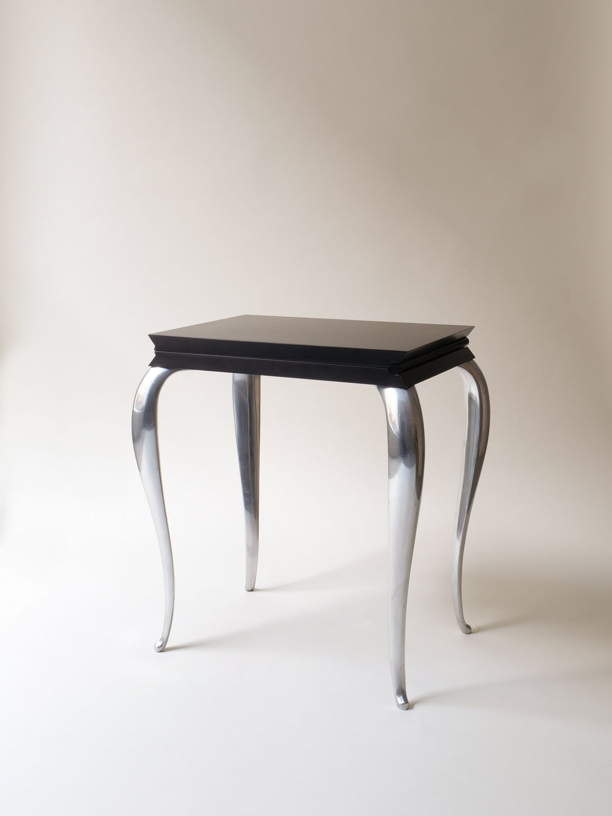 The "Lola Mundo Chair" by Philippe Starck from 1984, offered by Collection apart, has a glossy black top and four curvy metallic legs. Its elegant and modern style mirrors Louis XV design, making it perfect for collectors of exquisite furniture.