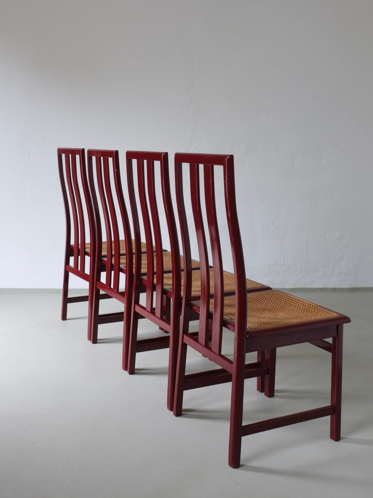 Four glossy wine red dining chairs with cane seats, rear angle view