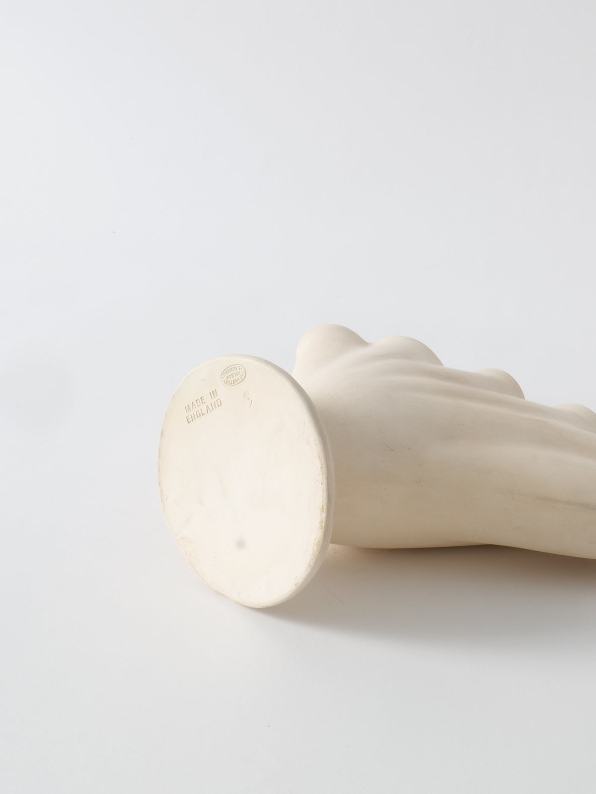 A white plaster Tulipiere Vase 1930s by Collection apart lies on its side against a plain white background. The flat, circular base of the vase displays some text and marks near the edge. The vase itself is smooth and slightly curved.
