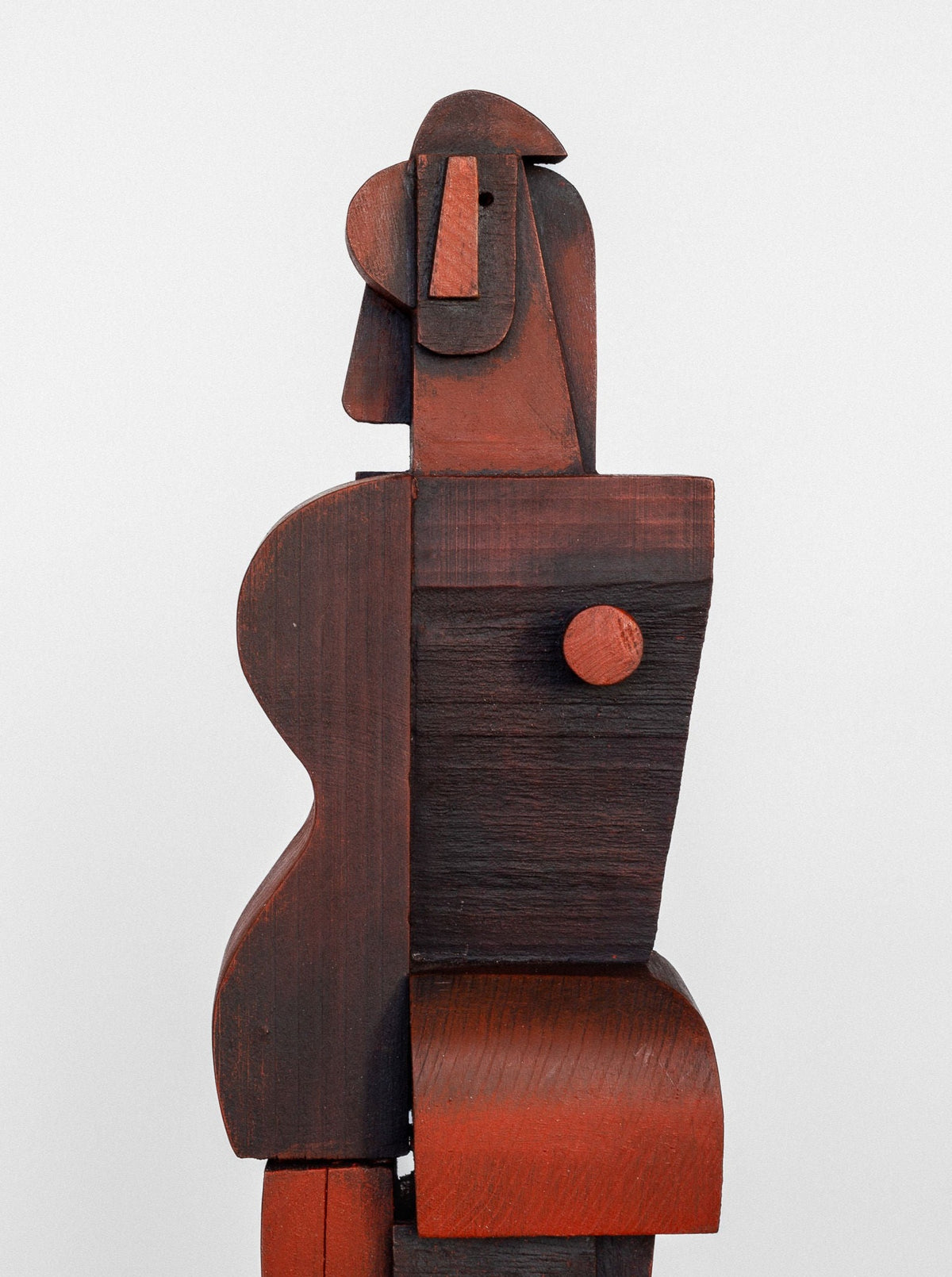 Introducing the Cubist Sculpture from Spigel by Atelier Boulogne: a wooden abstract piece featuring a stylized human figure in a cubist style. The sculpture is crafted from various rectangular and curved shapes in shades of brown and reddish tones, with a prominent cylindrical detail on the torso. The backdrop is plain and light-colored, enhancing its striking design.
