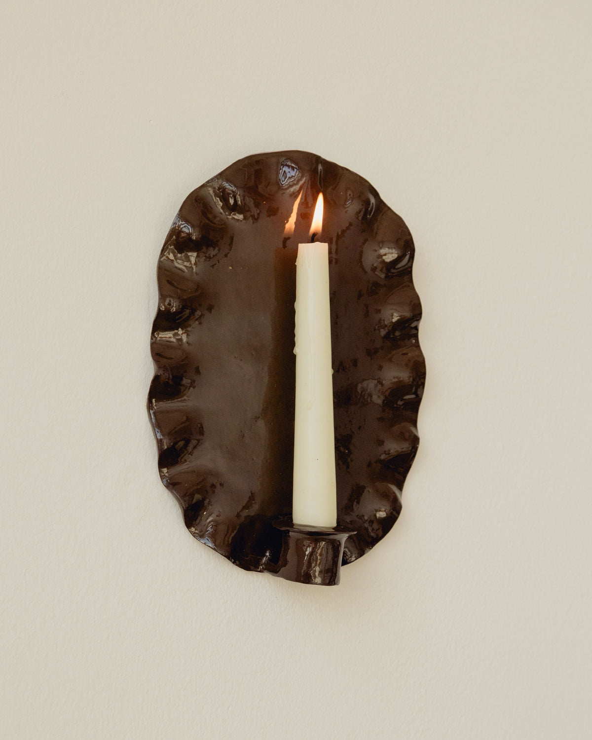 Ortigia oval bronze sconce with lit candle wall-mounted view