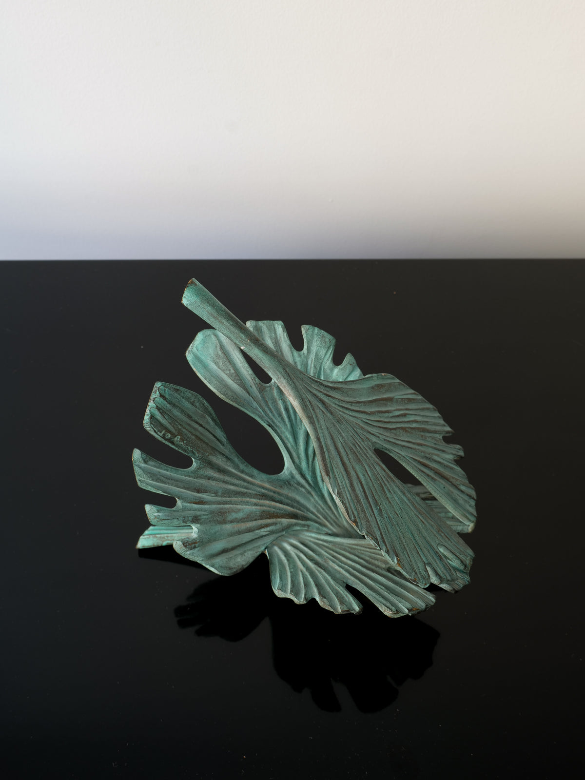 The Bronze Ginko Biloba Sculpture by Collection apart rests elegantly on a glossy black table, set against a plain white background.