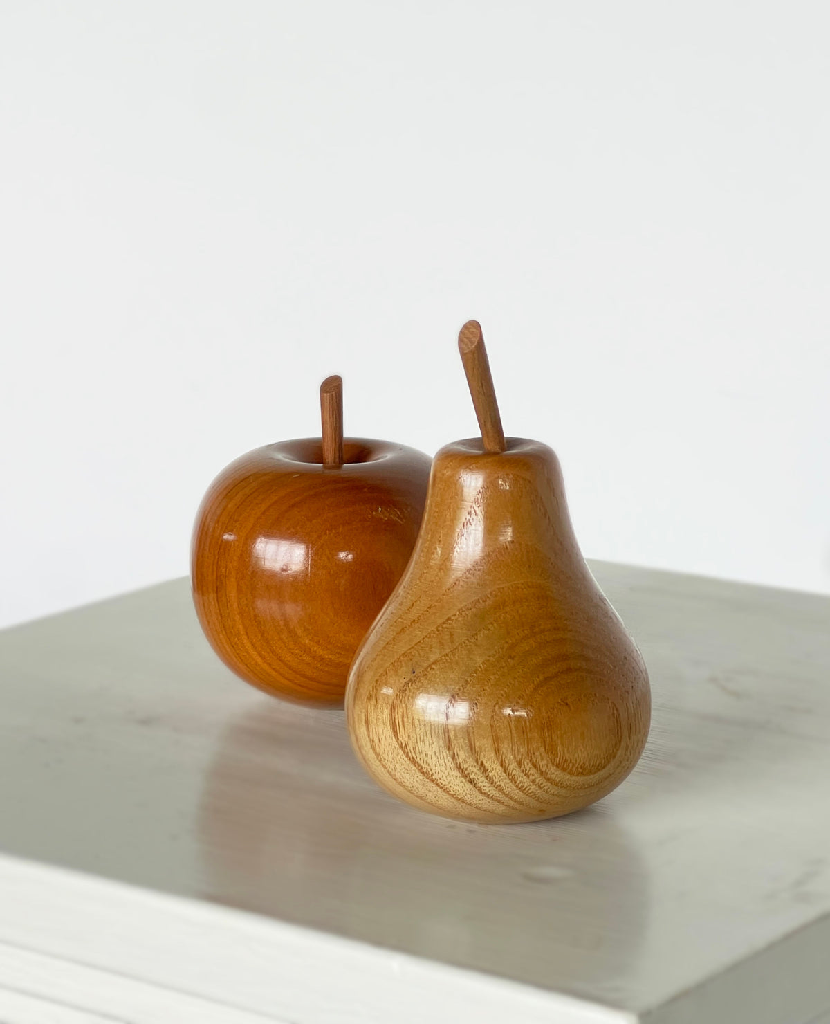 Polished wood apple and pear sculptures with stems on marble surface