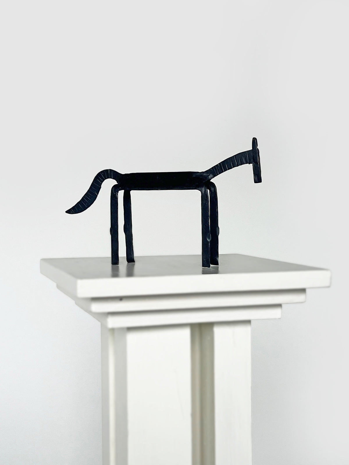Minimalist black iron horse sculpture on white pedestal